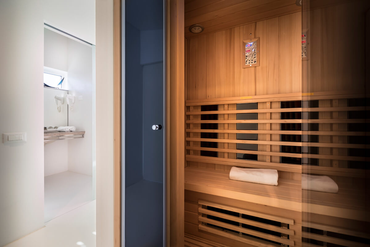 Sauna mit Holzbänken und zwei weißen Handtüchern, daneben heller Raum mit Waschbecken und Handtuchhalter