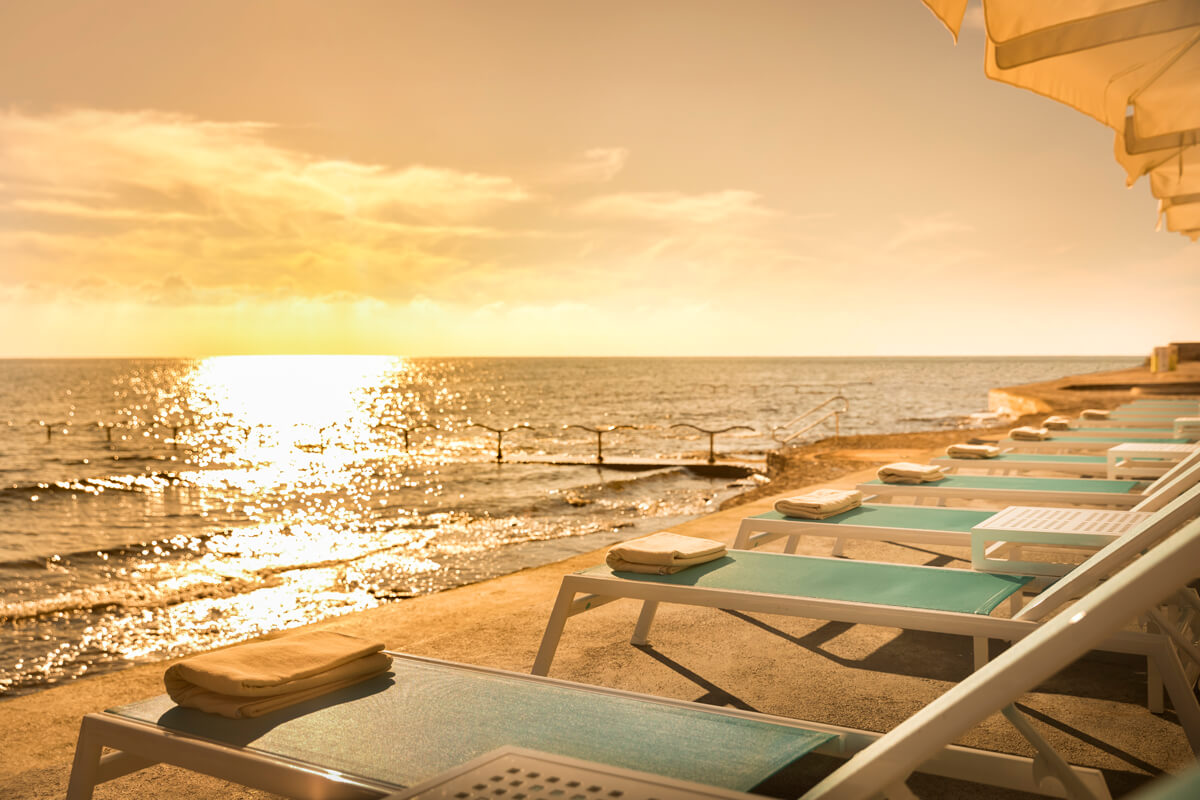 Sonnenuntergang über dem Meer mit Liegestühlen und Handtüchern am Strand