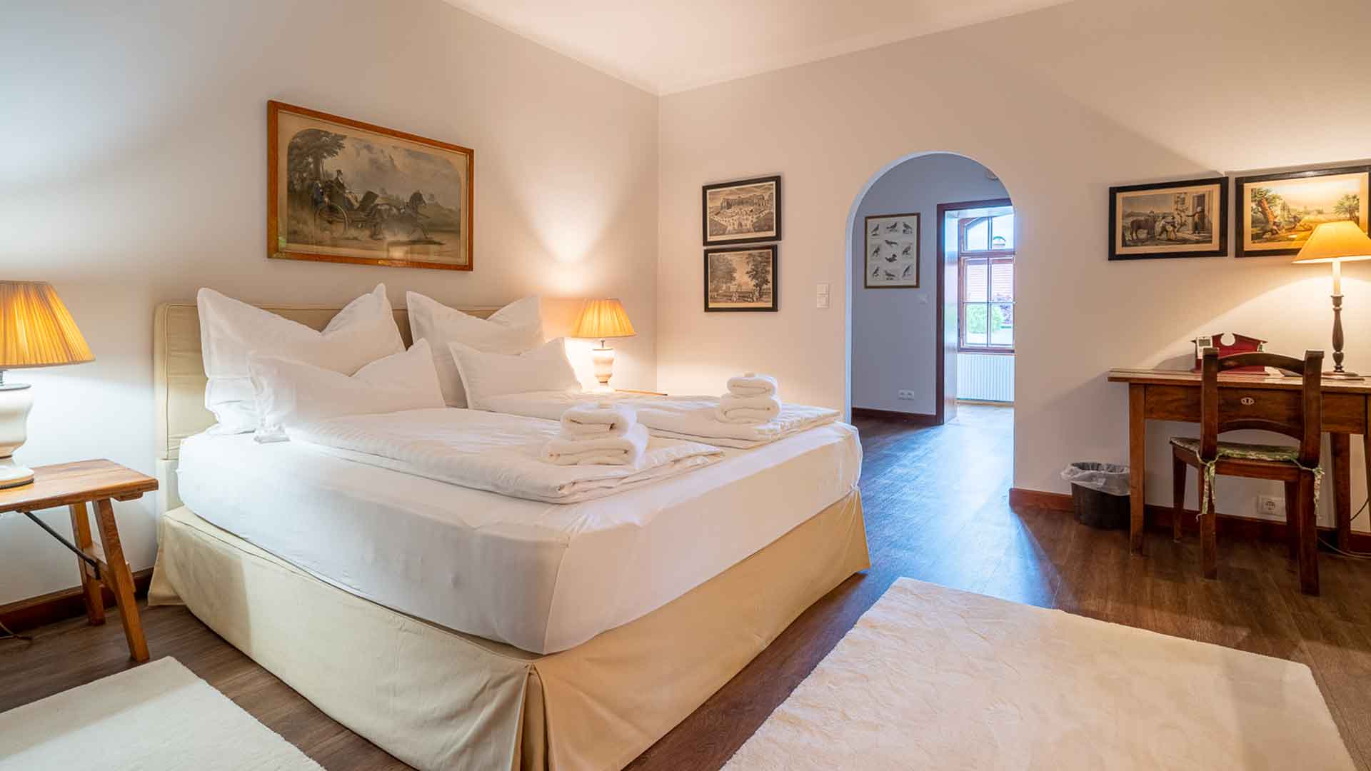 Helles Schlafzimmer mit Doppelbett, weicher Bettwäsche, Schreibtisch und klassischen Wandbildern.