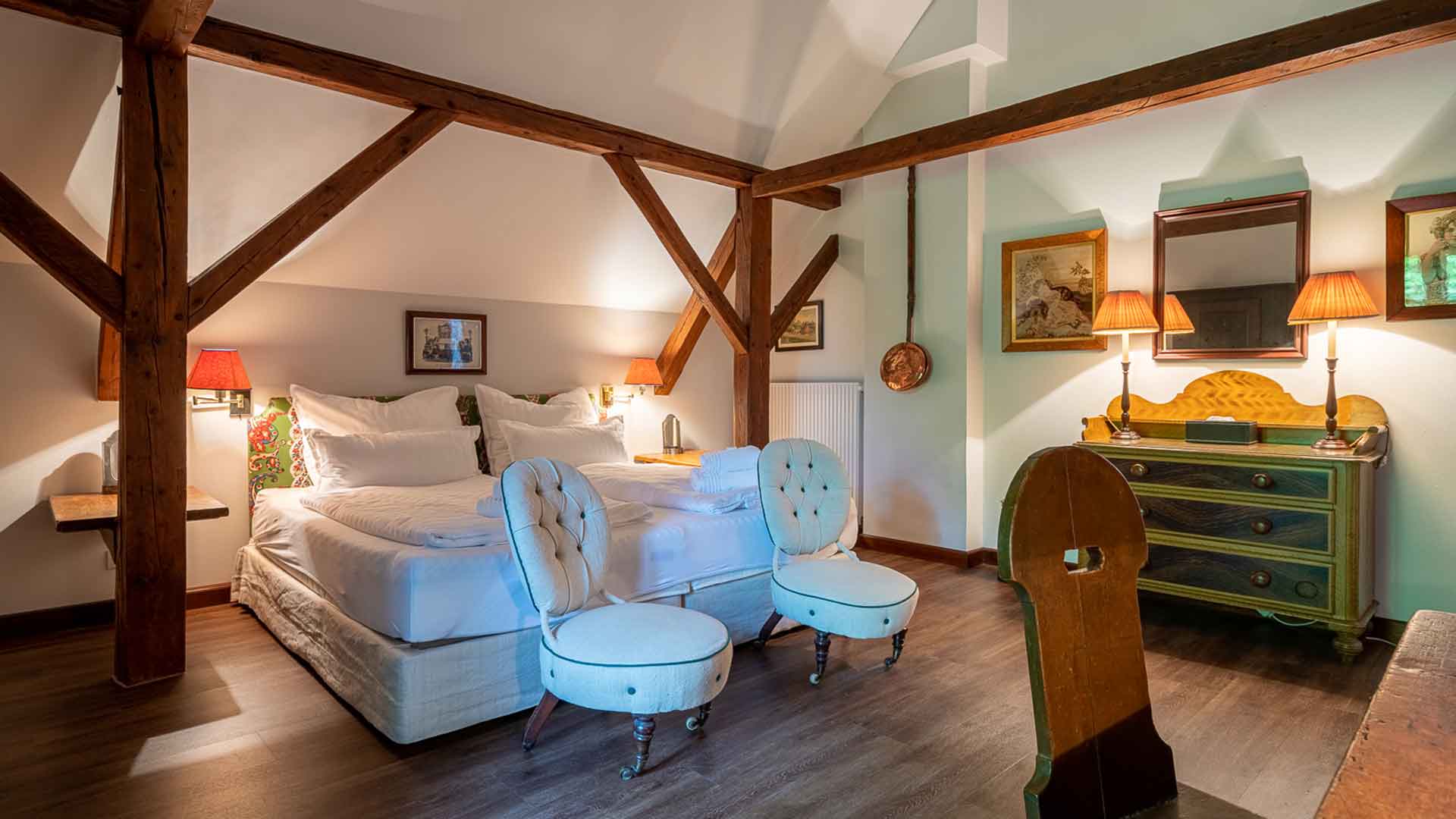 Charaktervolles Dachzimmer mit freiliegenden Holzbalken, Doppelbett, antiken Möbeln und gemütlicher Atmosphäre.