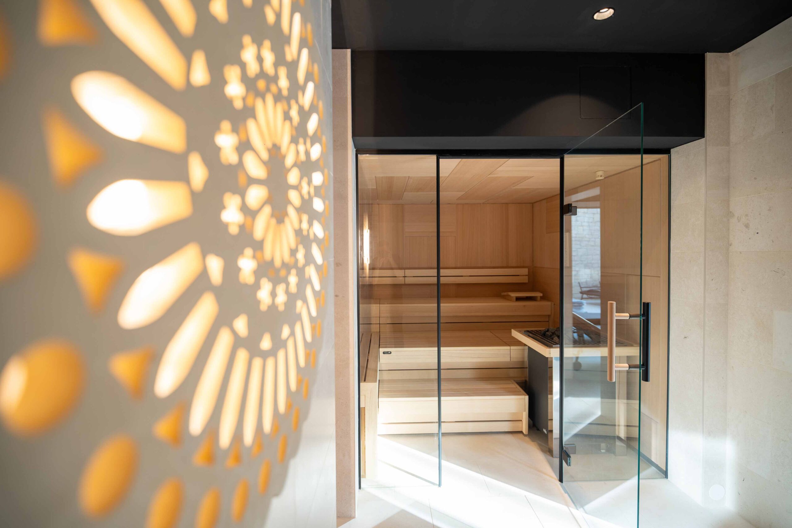 Moderne Sauna mit hellen Holzbänken, Glasfront und dekorativer Lichtinstallation an der Wand.