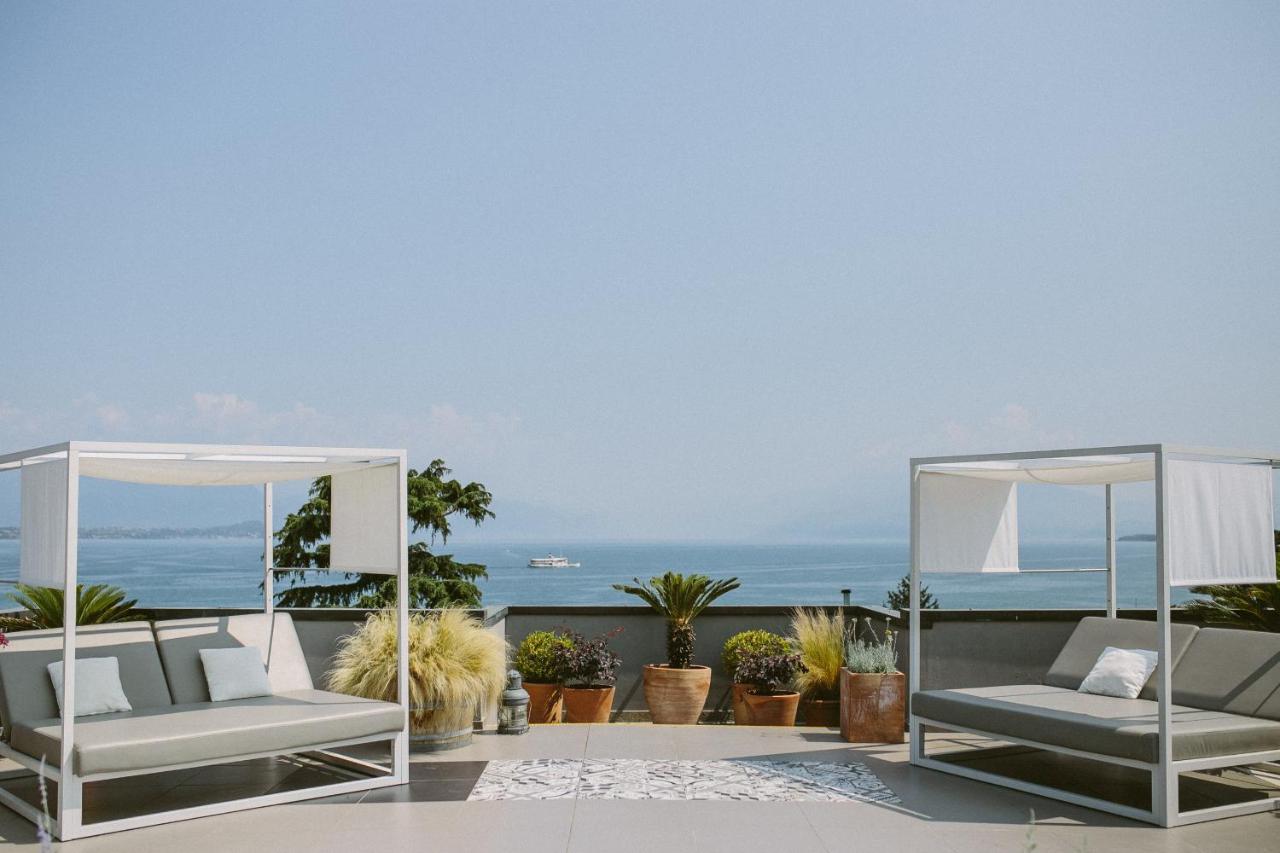 Moderne Dachterrasse mit zwei weißen, überdachten Lounge-Betten, Pflanzen in Töpfen und Ausblick auf den See mit vorbeifahrendem Boot.