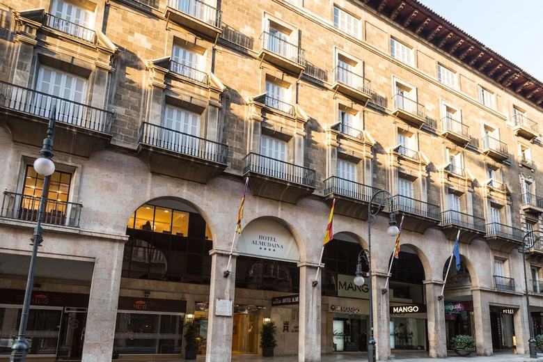 Fassade des Hotel Almudaina in Palma de Mallorca mit Arkadengang, Balkonen und Flaggen vor dem Eingang.