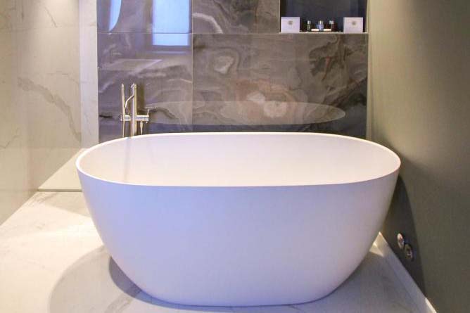 Modernes Badezimmer im Ambassador Palace Hotel mit freistehender Badewanne und Natursteinfliesen.