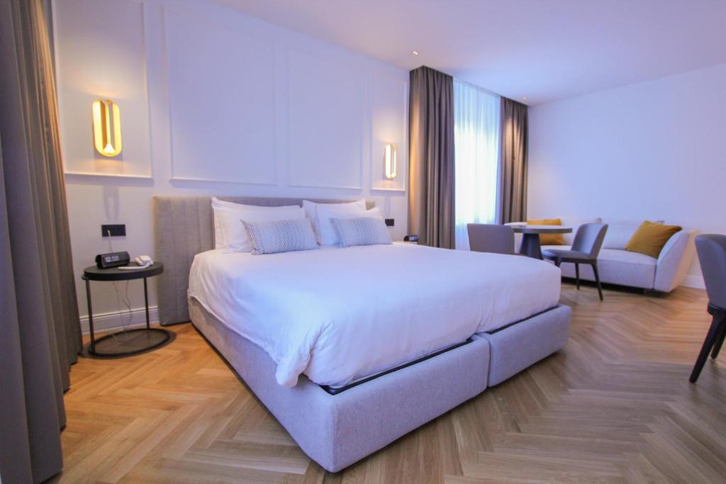 Großzügiges Hotelzimmer im Ambassador Palace Hotel mit Doppelbett, Sitzbereich und hellem Parkettboden.