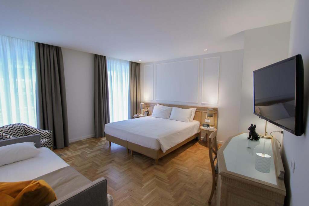 Geräumiges Mehrbettzimmer im Ambassador Palace Hotel mit zwei Betten, Schreibtisch und Tageslicht.