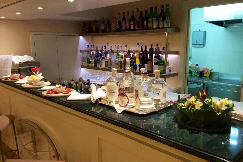 Hotelbar im Ambassador Palace Hotel mit Spirituosen, Desserts und direktem Blick in den Küchenbereich.