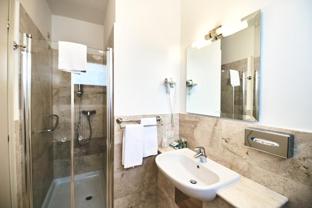 Badezimmer im Ambassador Palace Hotel mit Dusche, Waschbecken, Spiegel und Natursteinfliesen.