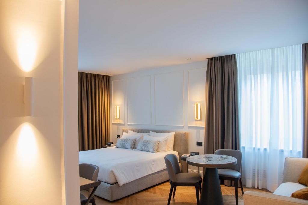 Helles Hotelzimmer im Ambassador Palace Hotel mit Doppelbett, Rundtisch und moderner Beleuchtung.