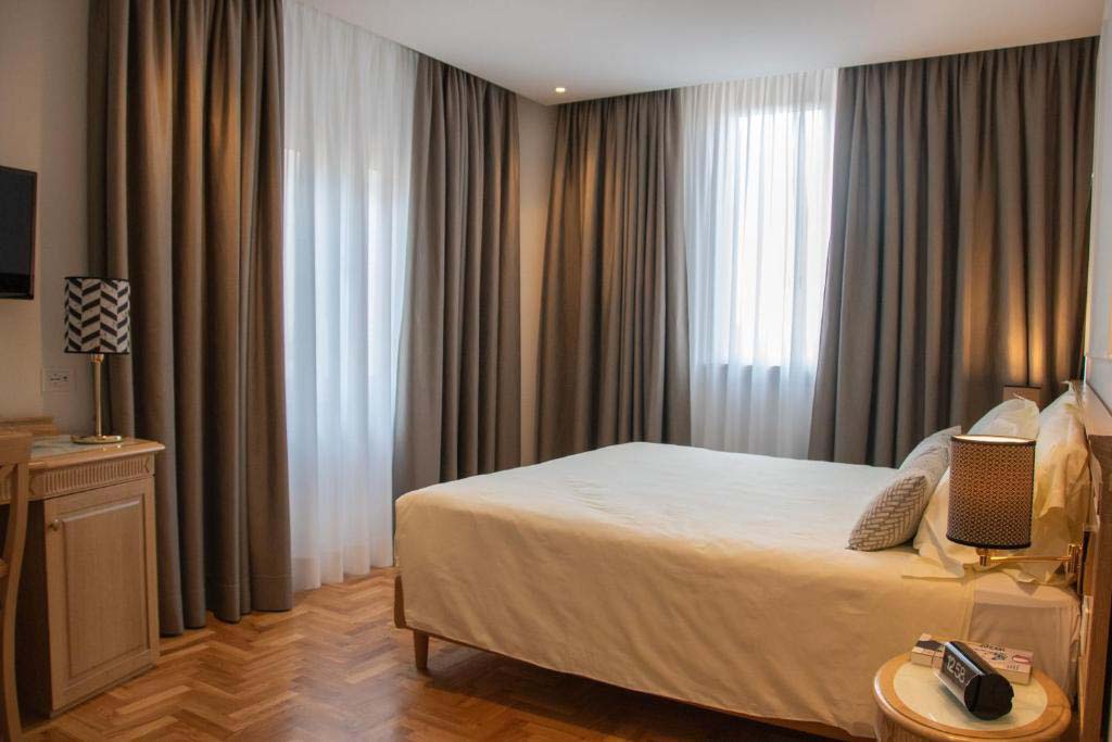 Klassisches Doppelzimmer im Ambassador Palace Hotel mit Holzboden, Nachttischen und Tageslicht.