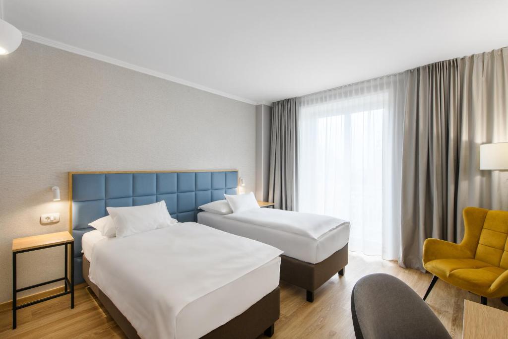 Modernes Zweibettzimmer im Eurostars uHotel mit zwei Einzelbetten, hellem Holzboden und bodentiefem Fenster für viel Tageslicht.