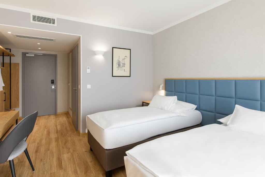 Helles Zweibettzimmer im Eurostars uHotel Ljubljana mit Schreibtisch, Garderobe und klarer, funktionaler Einrichtung.