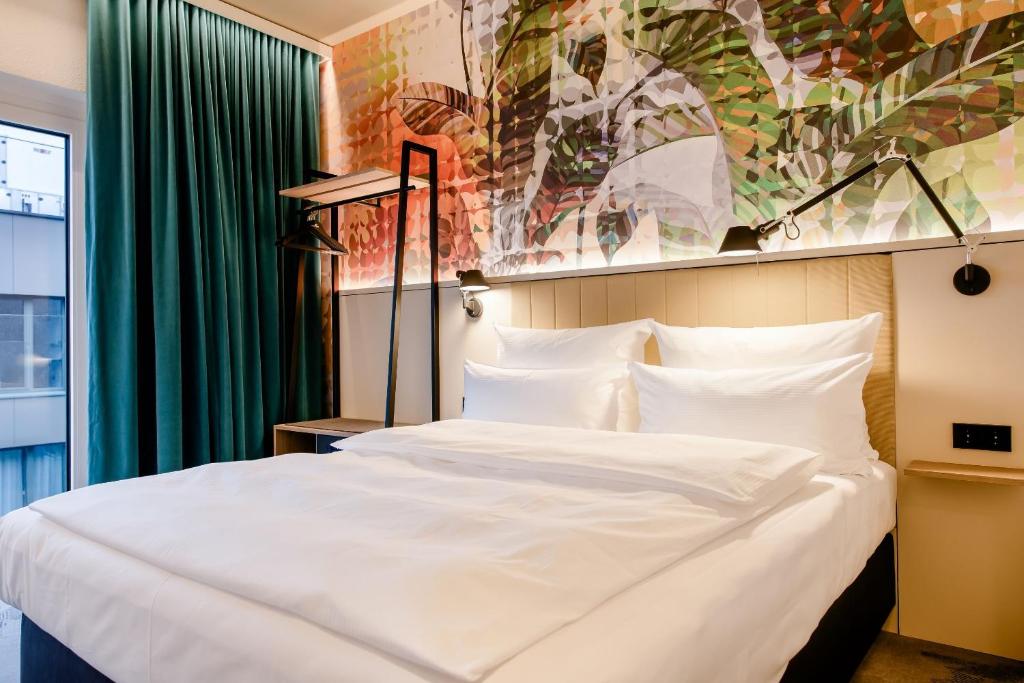 Modernes Hotelzimmer im Motel One Wien Donau City mit Doppelbett, Design-Wandgestaltung und bodentiefem Fenster für Tageslicht.