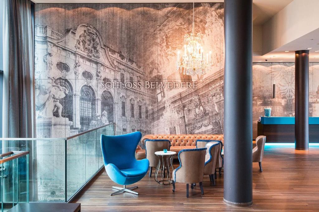 Lounge im Hotel Motel One Wien Hauptbahnhof mit Design-Sesseln und Wandmotiv Schloss Belvedere.