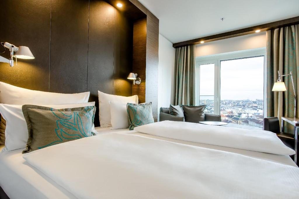 Modernes Hotelzimmer mit Doppelbett, Leselampen und Stadtblick im Motel One Wien Hauptbahnhof.