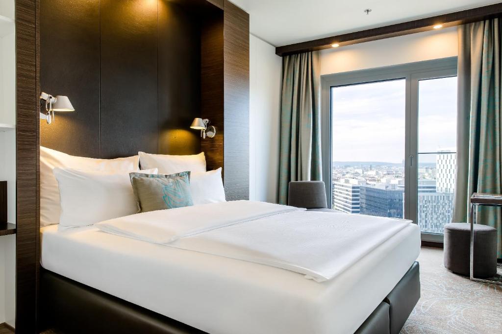 Hotelzimmer mit Doppelbett, Fensterfront und Blick über Wien im Motel One Wien Hauptbahnhof.