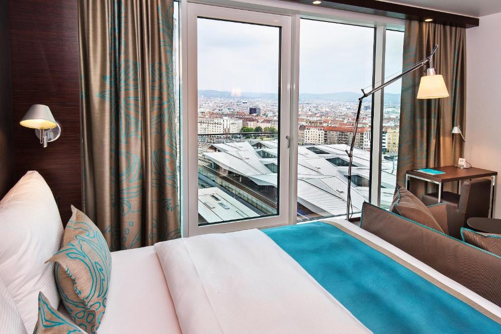 Modernes Hotelzimmer im Motel One Wien Hauptbahnhof mit Doppelbett, großem Fenster und Blick auf den Hauptbahnhof in Wien.