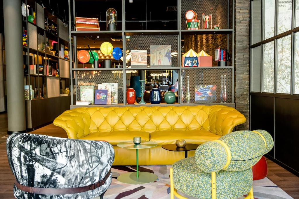 Stilvolle Lounge im Motel One Wien Prater mit gelbem Sofa, Designmöbeln und dekorativem Regal im Hintergrund.
