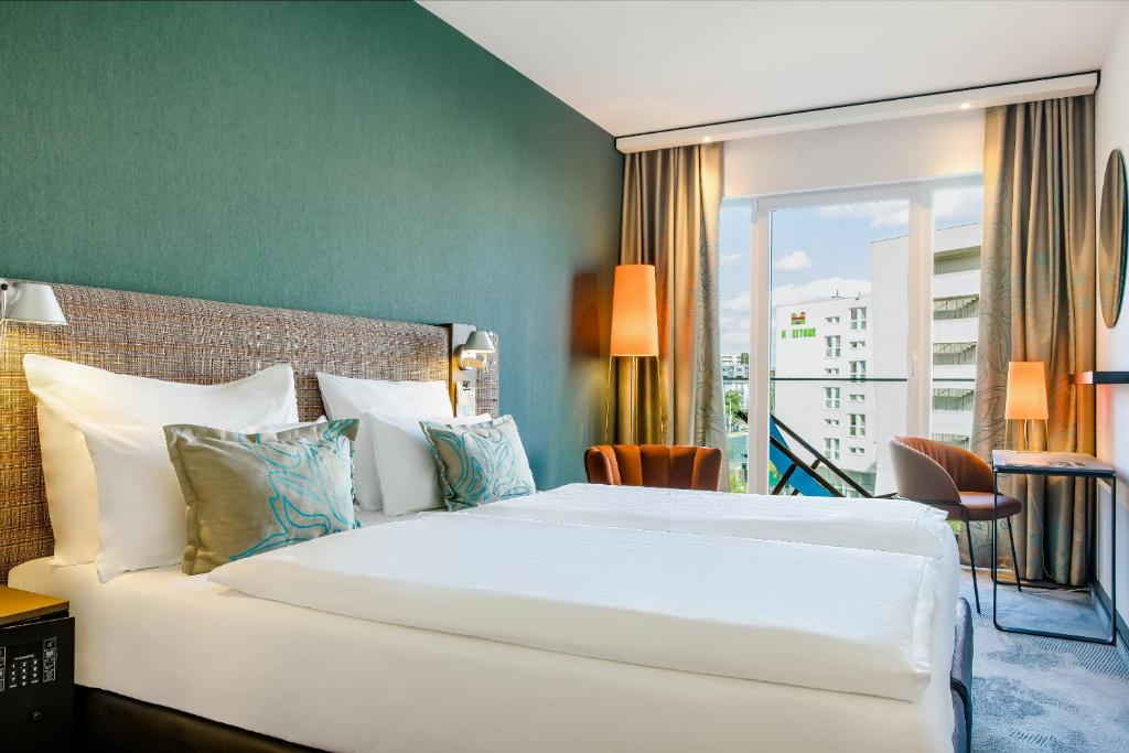 Modernes Doppelzimmer im Motel One Wien Prater mit großem Bett, Schreibtisch und Fensterfront mit Tageslicht.