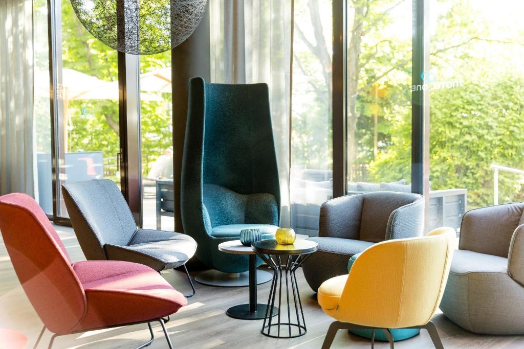 Lounge-Sitzbereich im Motel One Wien Prater mit farbigen Sesseln, Beistelltischen und bodentiefen Fenstern.