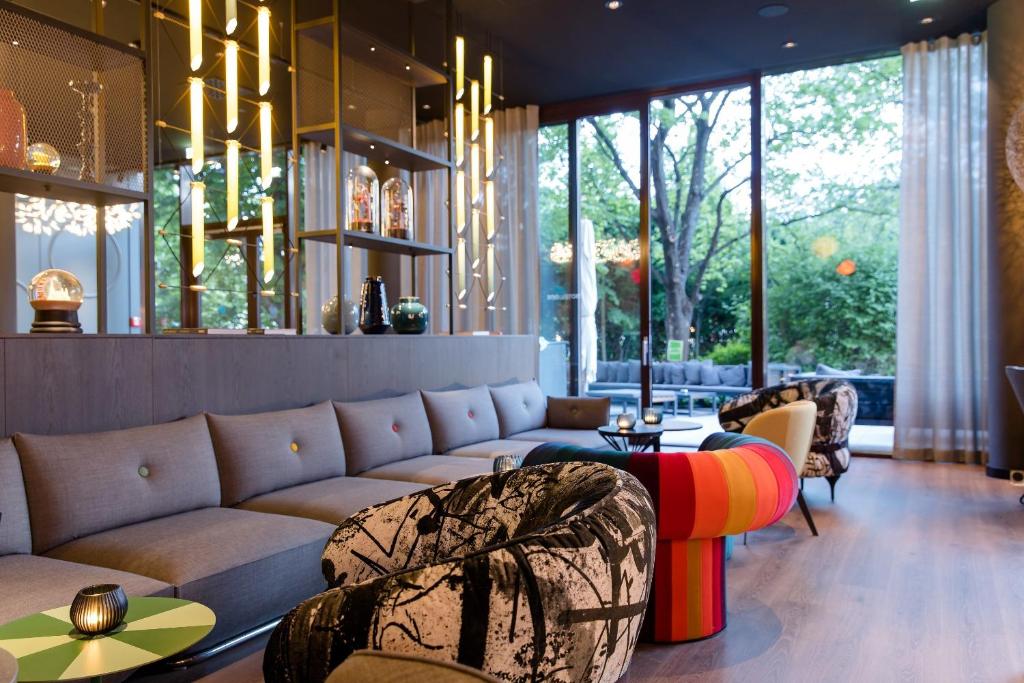 Großzügige Lobby im Motel One Wien Prater mit Sofalandschaft, Designmöbeln und Blick in den begrünten Außenbereich.