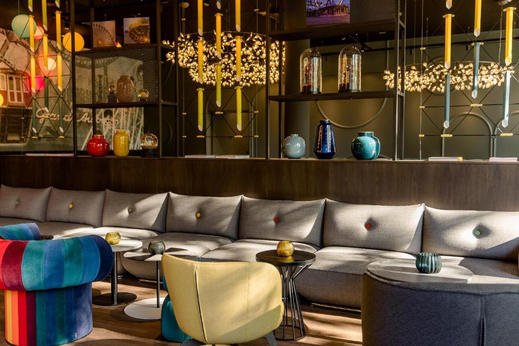 Moderne Lounge im Motel One Wien Prater mit grauem Sofa, bunten Sesseln, kleinen Beistelltischen und dekorativer Beleuchtung.