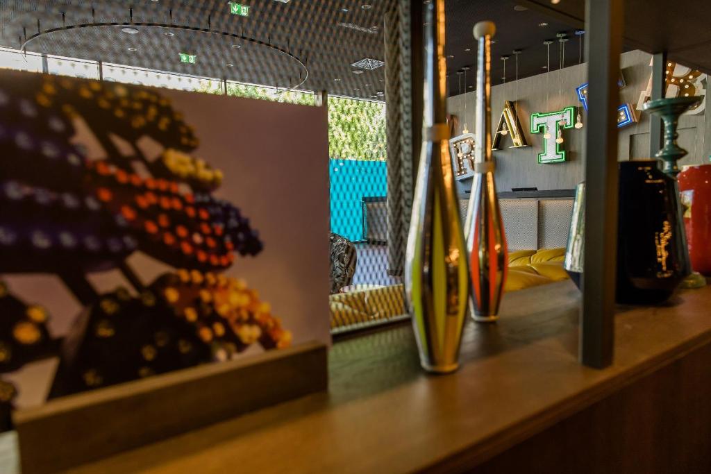 Blick durch ein offenes Regal im Motel One Wien Prater mit Designvasen, Büchern und Blick auf die gemütliche Lounge im Hintergrund.