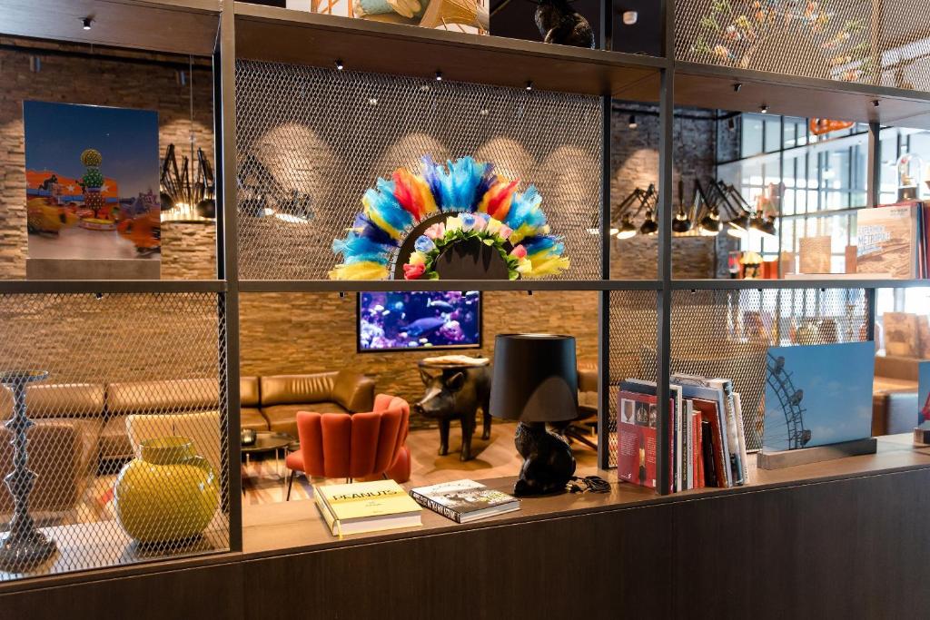 Dekoratives Regal im Motel One Wien Prater mit buntem Federschmuck, Designobjekten und gemütlicher Lounge im Hintergrund.