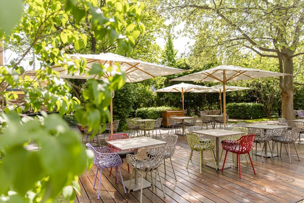 Großzügige Terrasse im Motel One Wien Prater mit Tischen, Stühlen, Sonnenschirmen und Blick ins begrünte Gartenareal.