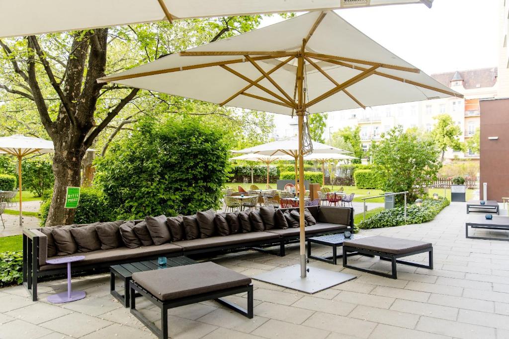 Ruhige Gartenterrasse des Motel One Wien Prater mit Sitzlounge, Sonnenschirmen und grüner Umgebung.