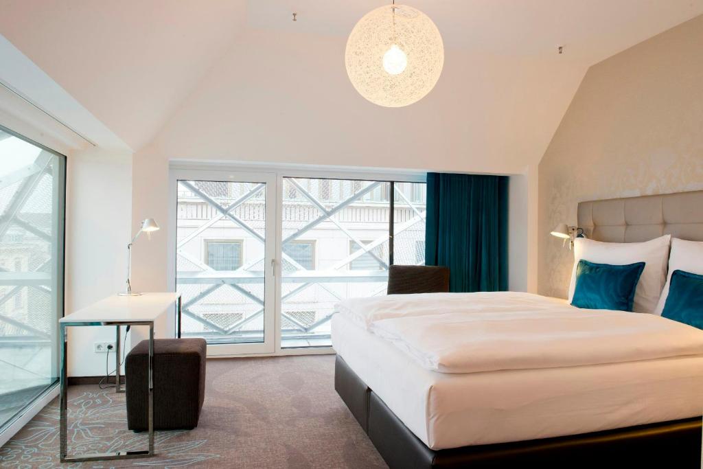 Modernes Hotelzimmer im Motel One Wien Staatsoper mit komfortablem Bett, großem Fenster, Design-Leuchten und ruhiger Atmosphäre.