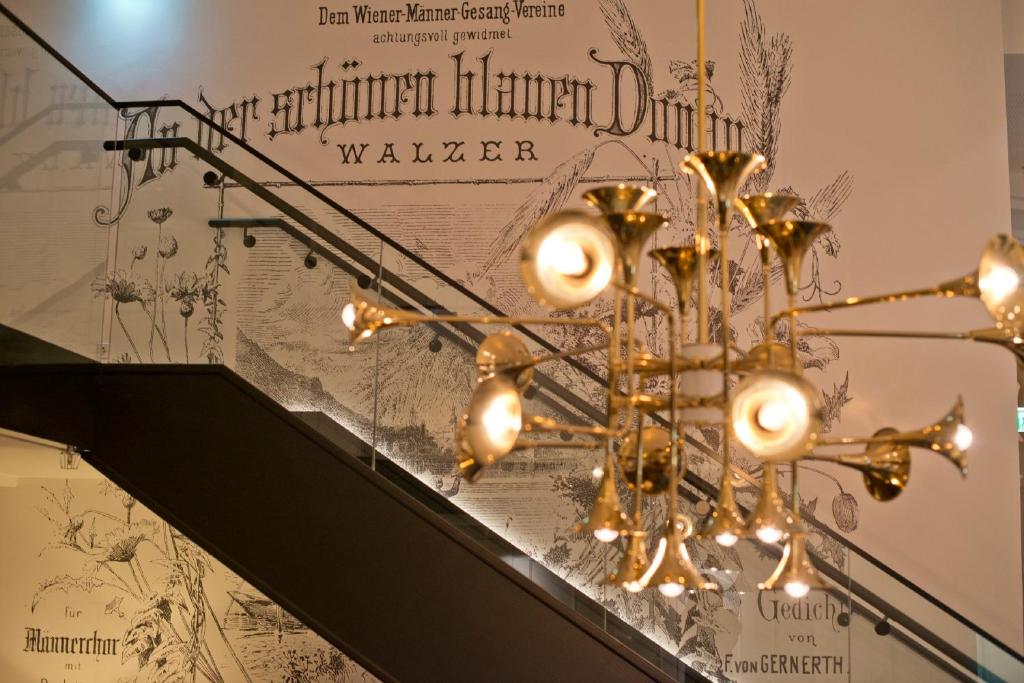 Design-Detail im Motel One Wien Staatsoper mit Treppenaufgang, moderner Leuchte und kunstvoll gestalteter Wandgrafik.
