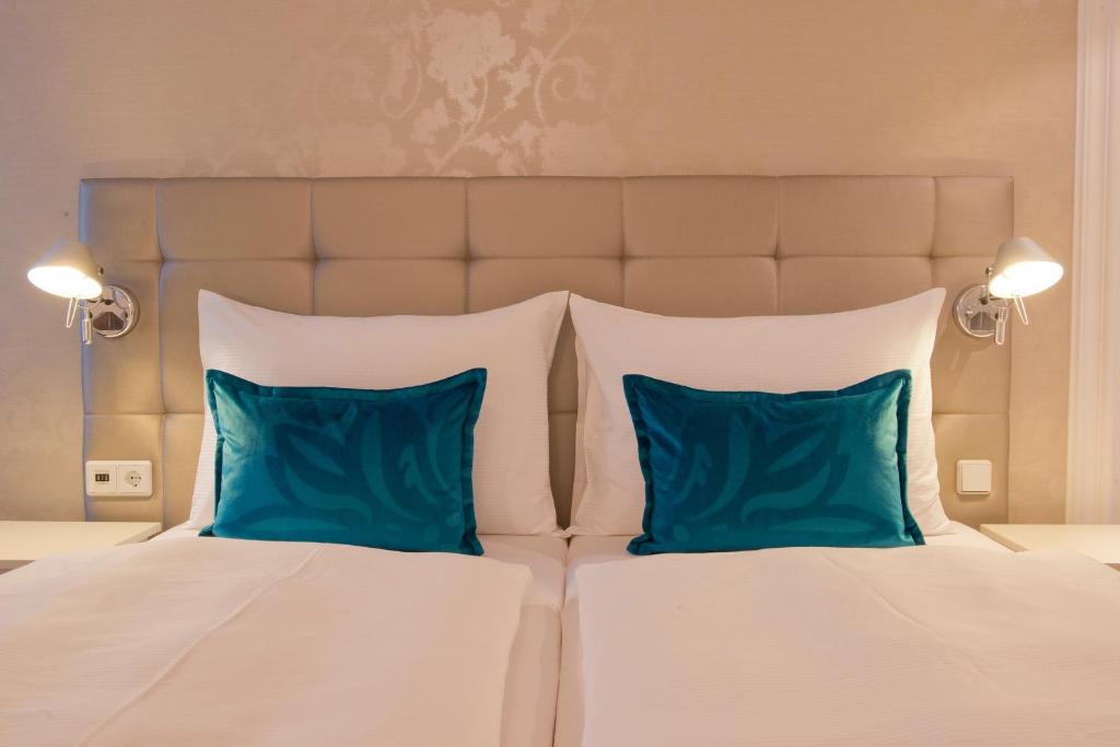 Detailansicht des komfortablen Doppelbetts im Motel One Wien Staatsoper mit gepolstertem Kopfteil, Leselampen und türkisfarbenen Kissen.