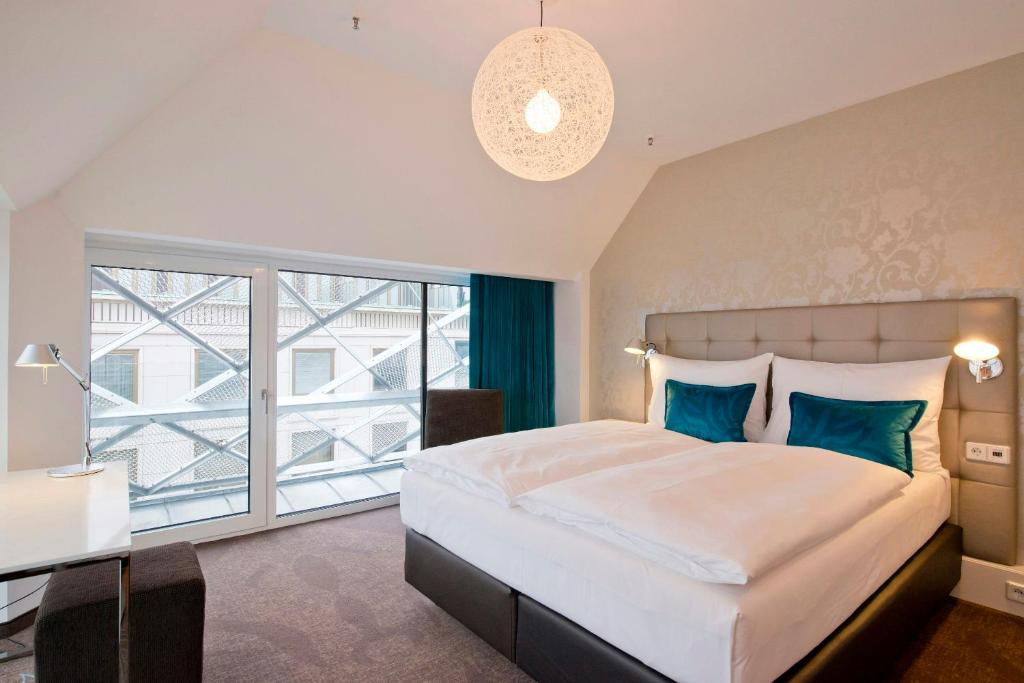 Geräumiges Design-Zimmer im Motel One Wien Staatsoper mit Doppelbett, Schreibtisch, bodentiefen Fenstern und moderner Innenarchitektur.