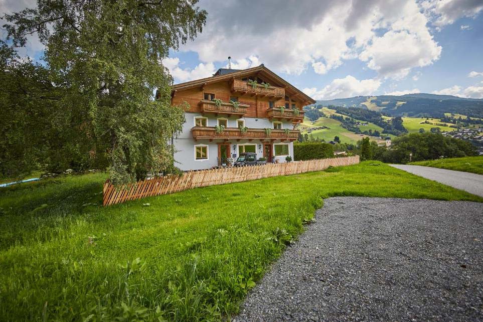 Außenansicht der Pension Enzian in ruhiger Lage, umgeben von grünen Wiesen und alpiner Berglandschaft.