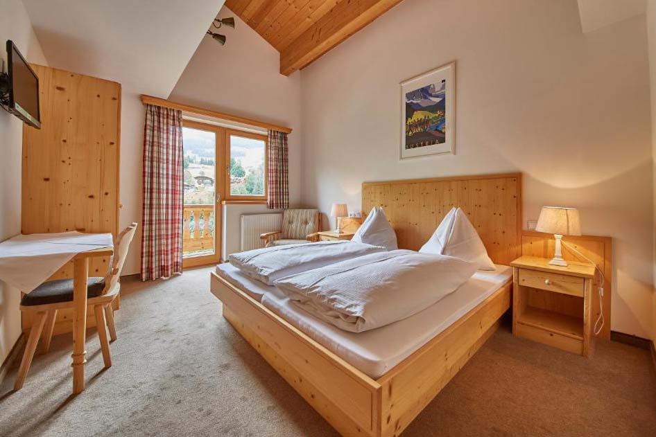 Helles Doppelzimmer in der Pension Enzian mit Holzmöbeln, Balkon und Blick auf die umliegende Berglandschaft.