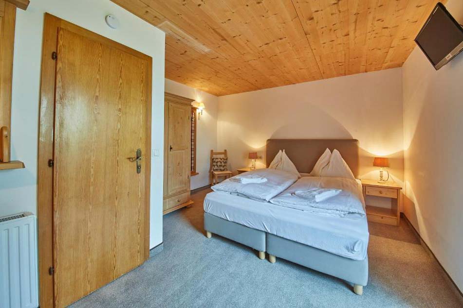 Gemütliches Doppelzimmer in der Pension Enzian mit Holzdecke, komfortablem Bett und warmem Licht.