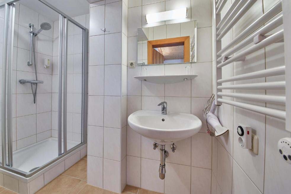 Badezimmer in der Pension Enzian mit Dusche, Waschbecken und heller Fliesenoptik.