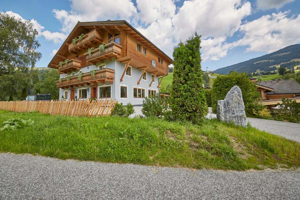 Pension Enzian mit traditioneller Holzfassade in sonniger Lage vor alpiner Kulisse.