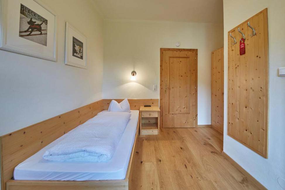 Einzelzimmer in der Pension Enzian mit Holzboden, Einzelbett und funktionaler Ausstattung.