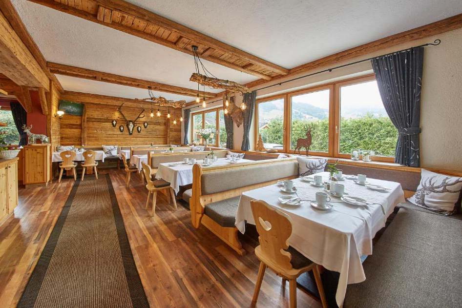 Heller Frühstücksraum der Pension Enzian mit viel Holz, gedeckten Tischen und Blick auf die umliegende Berglandschaft.