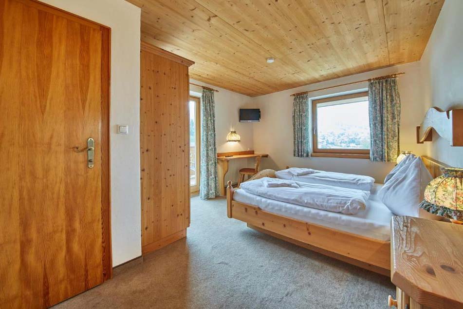Gemütliches Doppelzimmer in der Pension Enzian mit Holzmöbeln, Schreibtisch und Blick ins Tal.