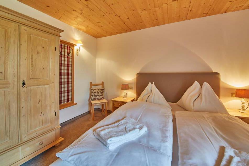 Traditionell eingerichtetes Doppelzimmer in der Pension Enzian mit Holzdecke und warmem Licht.