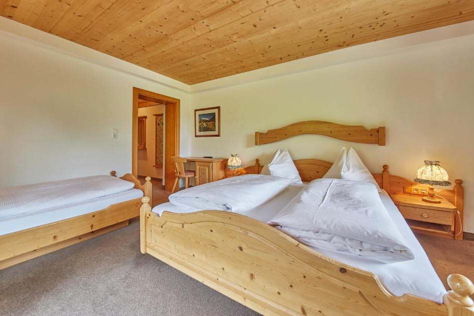 Geräumiges Mehrbettzimmer in der Pension Enzian mit Holzmöbeln, ideal für Familien oder Gruppen.