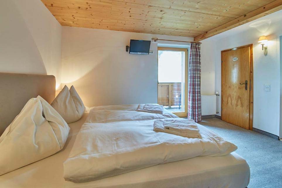 Doppelzimmer in der Pension Enzian mit Balkon, Holzausstattung und Blick auf die umliegende Berglandschaft.