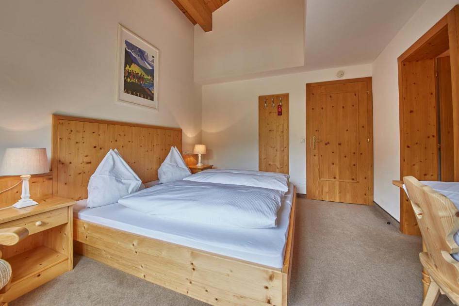 Helles Doppelzimmer in der Pension Enzian mit komfortablem Bett, Holzmöbeln und gemütlicher Atmosphäre.