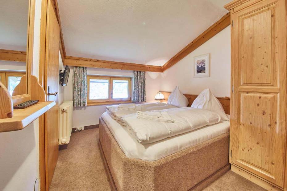Gemütliches Doppelzimmer in der Pension Enzian mit Holzmöbeln, Doppelbett und Fenster zur ruhigen Bergseite.