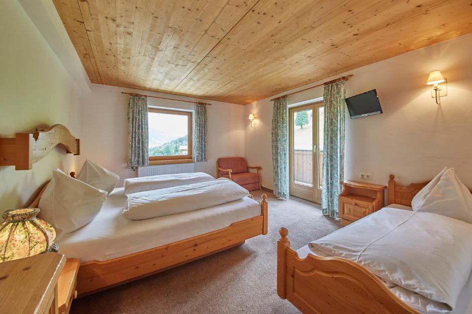Geräumiges Mehrbettzimmer in der Pension Enzian mit Holzdecke, mehreren Betten und Balkonzugang.