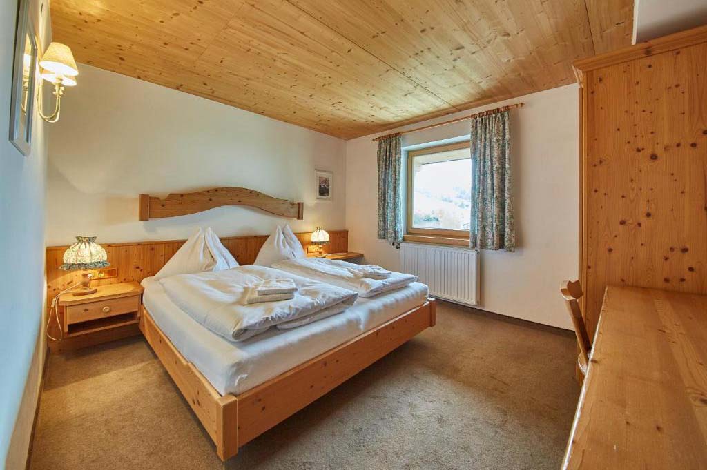 Klassisch eingerichtetes Doppelzimmer in der Pension Enzian mit Holzbett, Nachttischen und warmem Licht.