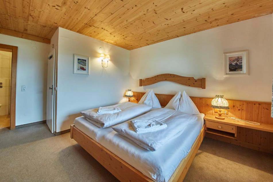 Helles Doppelzimmer in der Pension Enzian mit komfortablem Bett, Holzdecke und Blick ins Grüne.